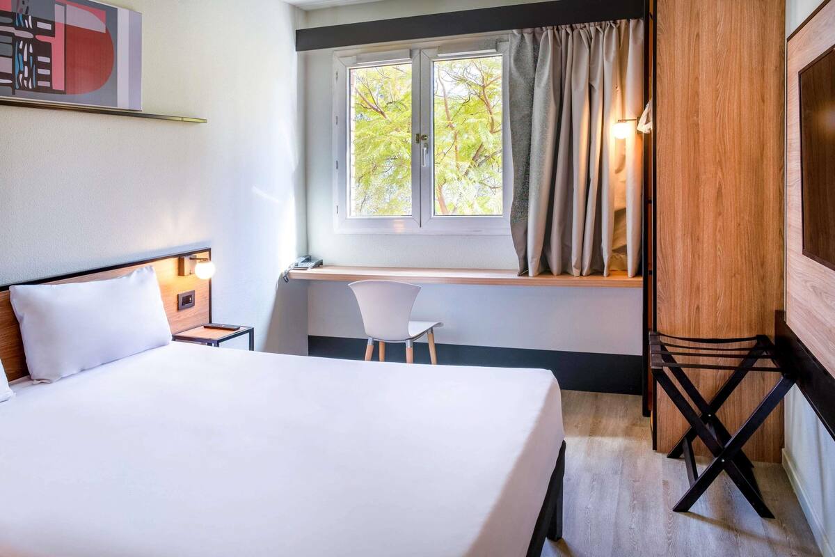 Een hotelkamer met een bed, een bureau, een stoel en een raam met gordijnen.