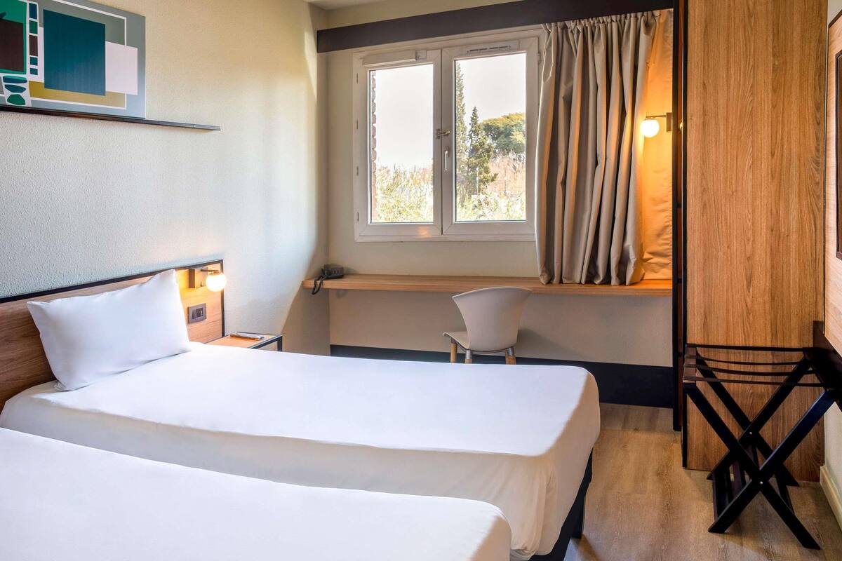 Een hotelkamer met twee bedden, een bureau, een stoel en een raam met gordijnen.