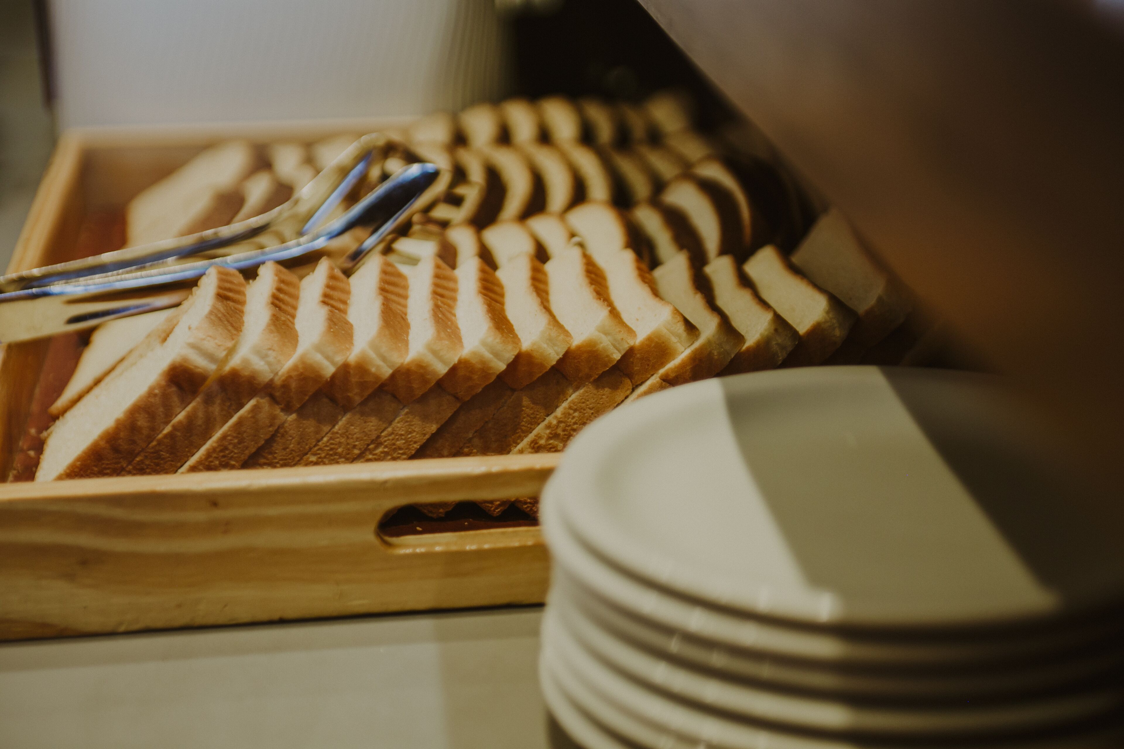 A wooden tray with sliced bread and a stack of white plates.