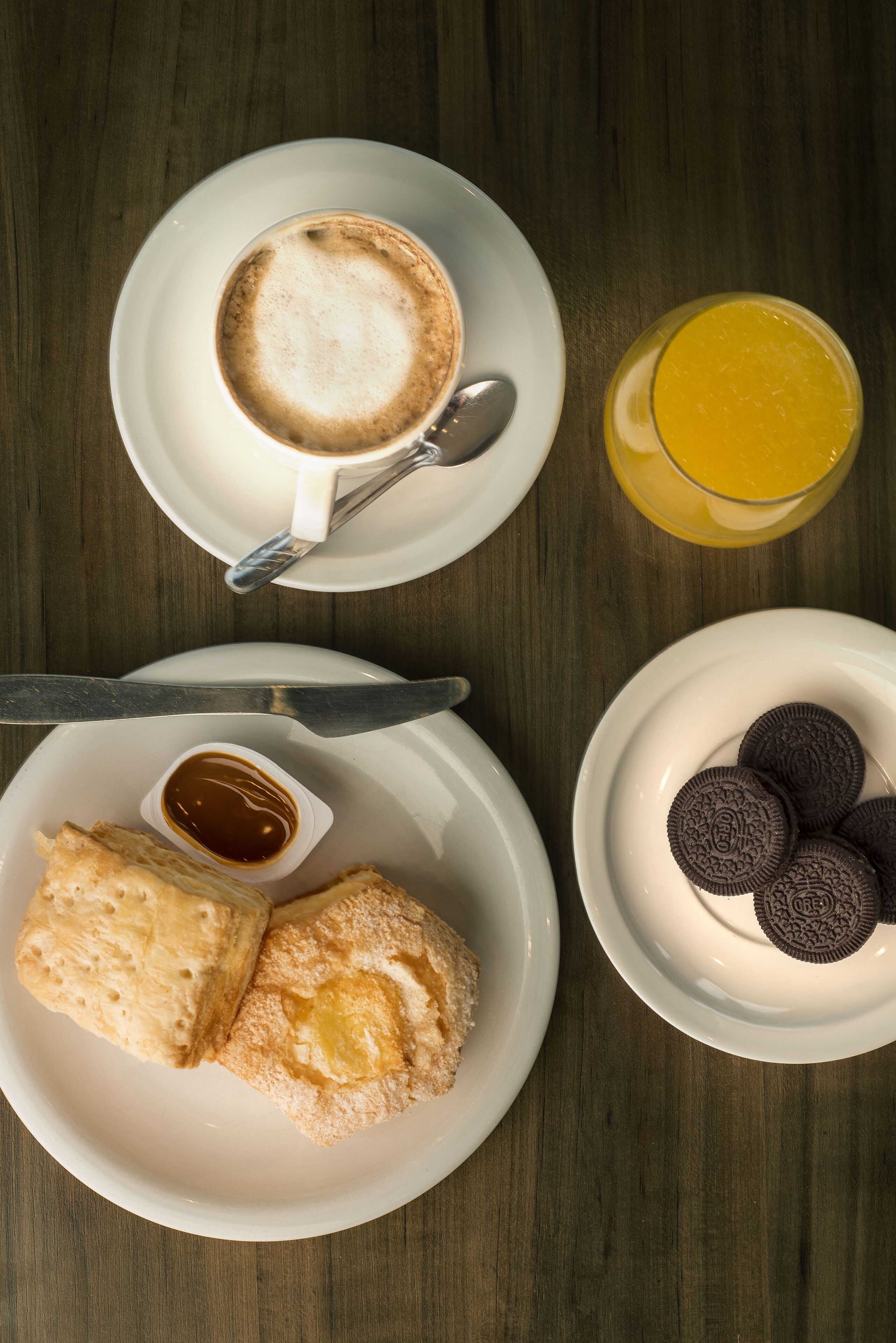 A breakfast setting with a cup of coffee, a glass of orange juice, biscuits, a plate of cookies, and a small bowl of jam.