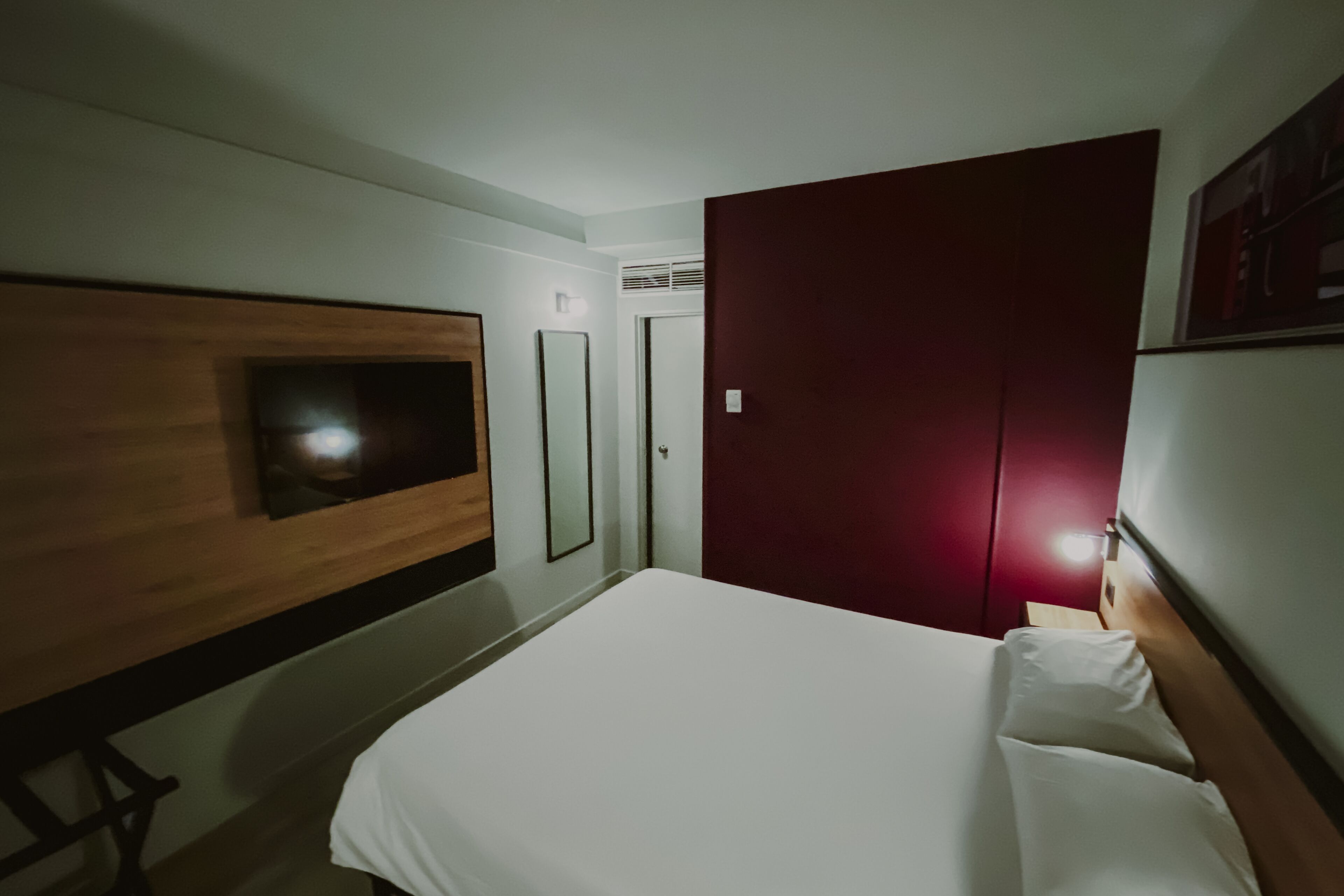 Habitació d'hotel amb un llit, una televisió penjada a la paret, un armari i una porta.