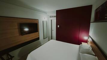 Habitació d'hotel amb un llit, una televisió penjada a la paret, un armari i una porta.