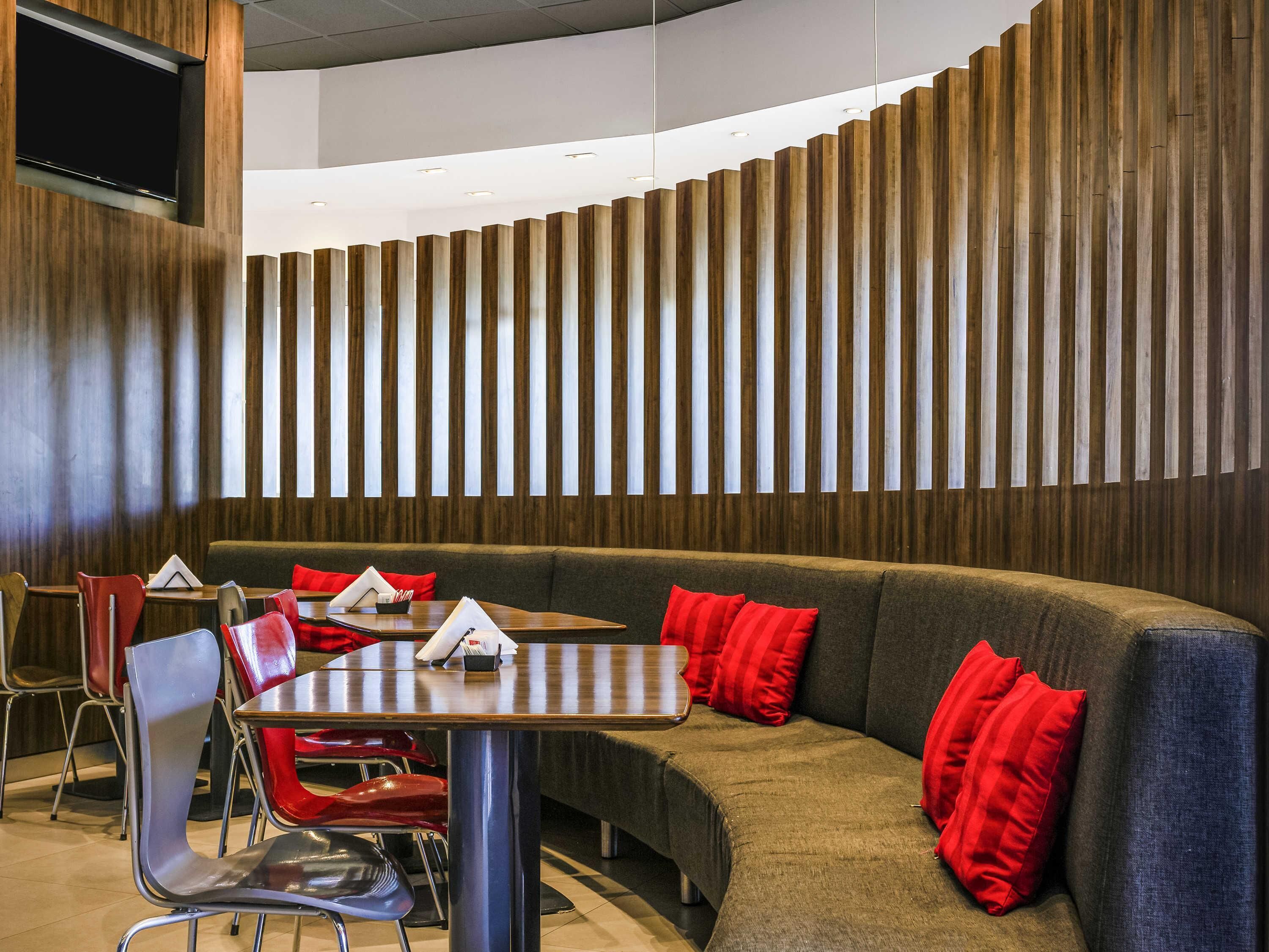 Un restaurante moderno con una zona de estar curva, pared de paneles de madera y cojines rojos.
