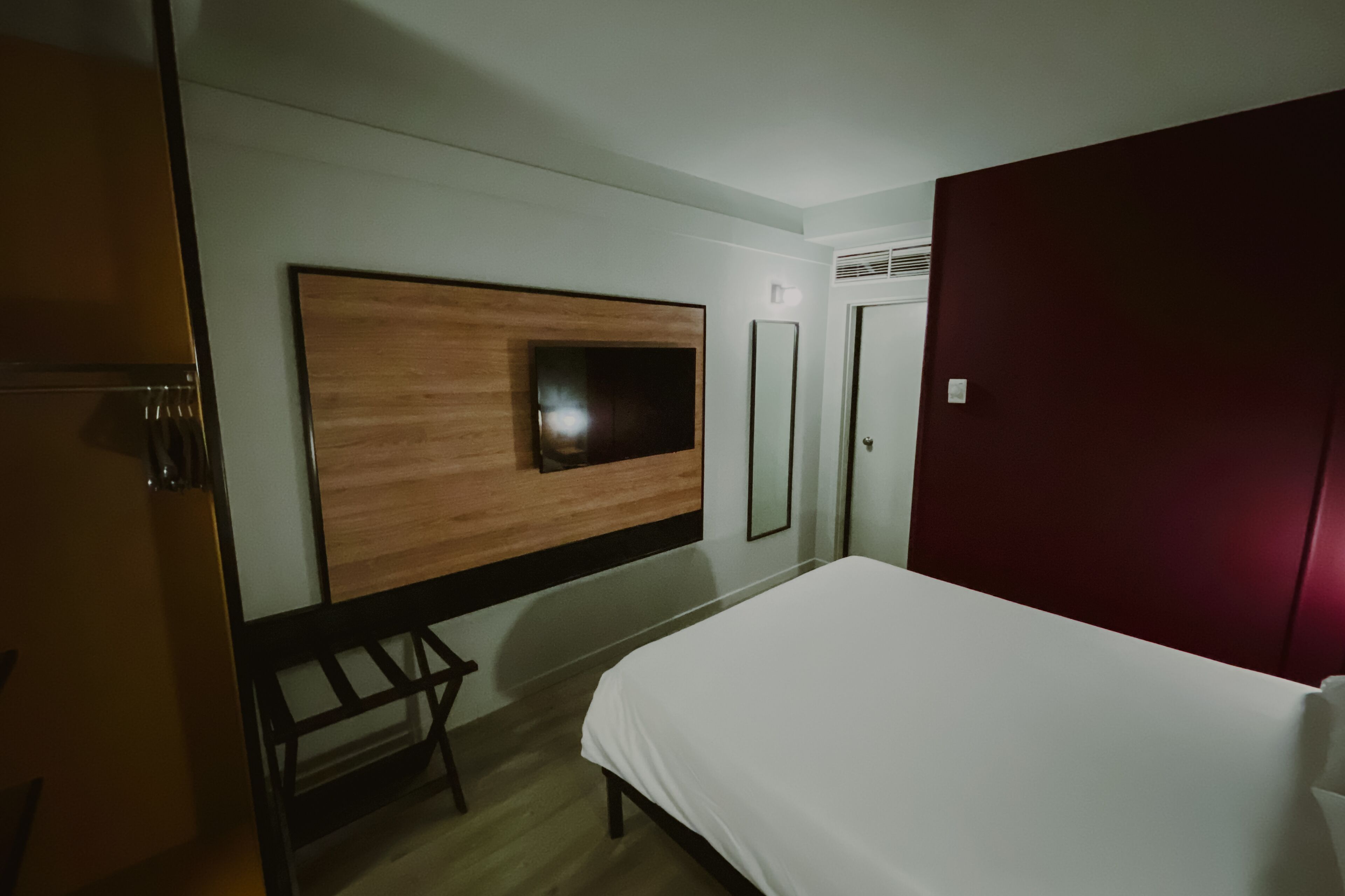 A hotel room with a bed, a wooden panel wall, a TV, and a red wardrobe.