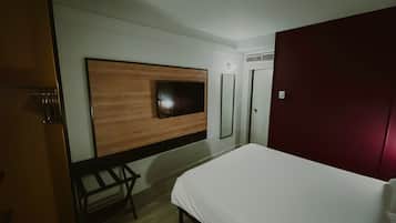 Quarto de hotel com cama, parede de painéis de madeira, televisão e guarda-roupa vermelho.