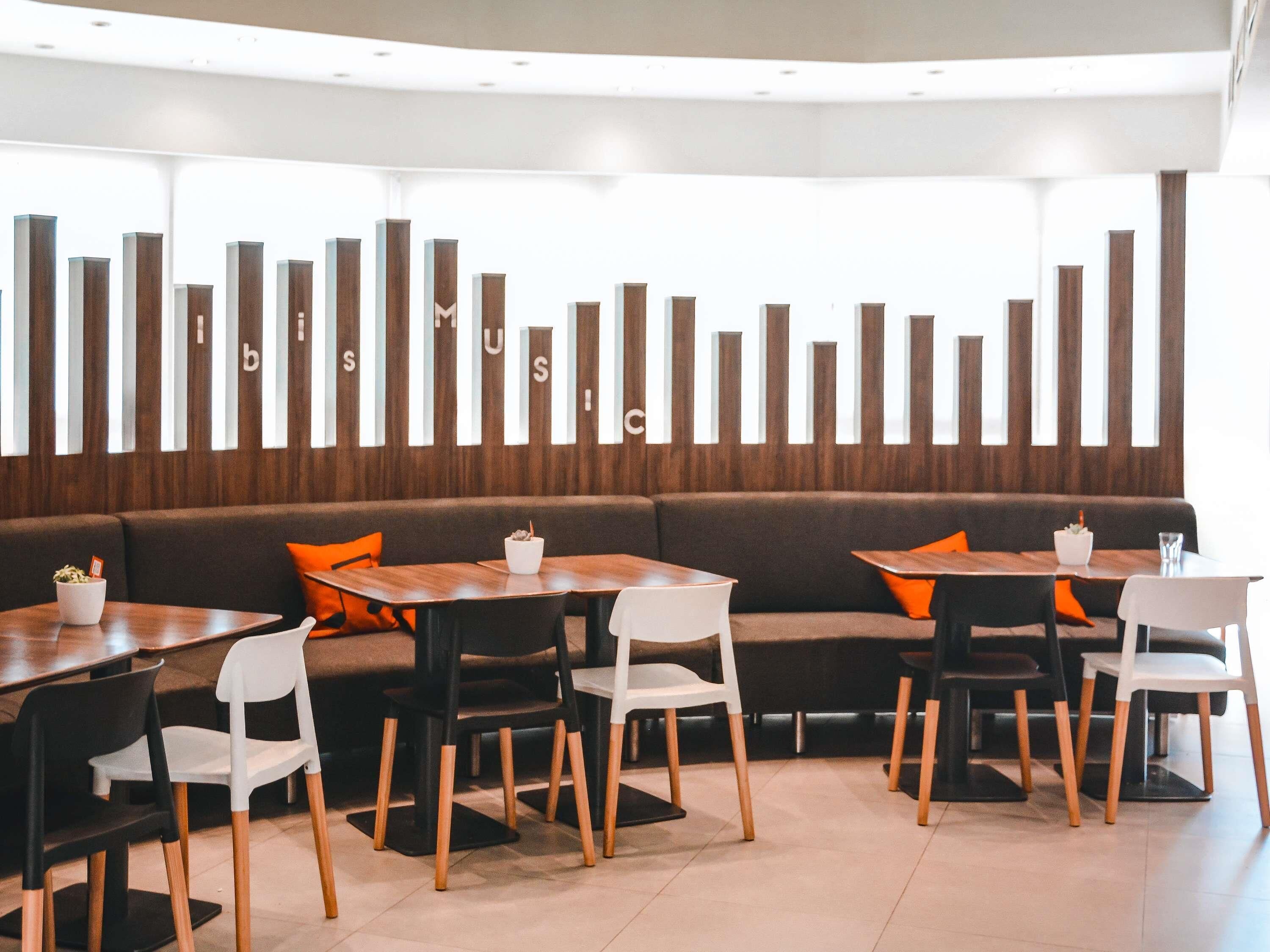 En modern restaurang med en lång bardisk, flera olika sittalternativ, inklusive en soffa och stolar, samt en dekorativ vägg med vertikala element.