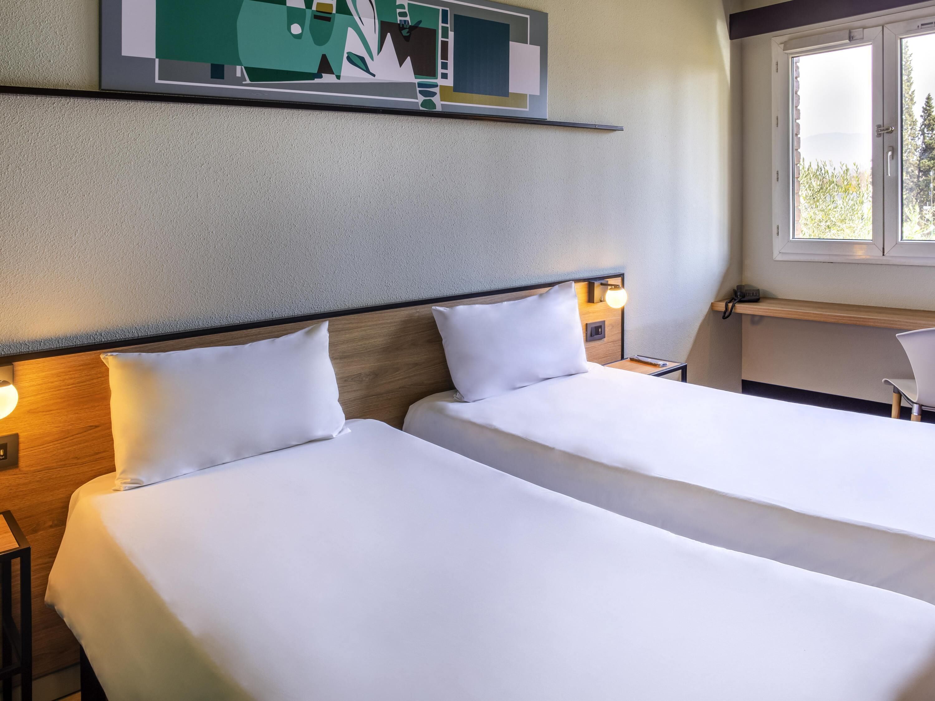 A hotel room with two beds, a desk, a chair, and a window with a view.