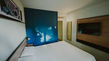 Habitación de hotel con cama, televisor de pared y ventana grande con vistas al exterior.