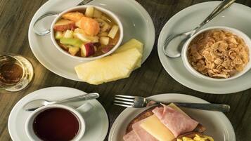 A breakfast setting with a bowl of fruit, a cup of coffee, cereal, toast with cheese and ham, and a glass of juice.