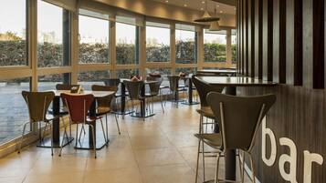 A modern bar with large windows, metal chairs, and a tiled floor.