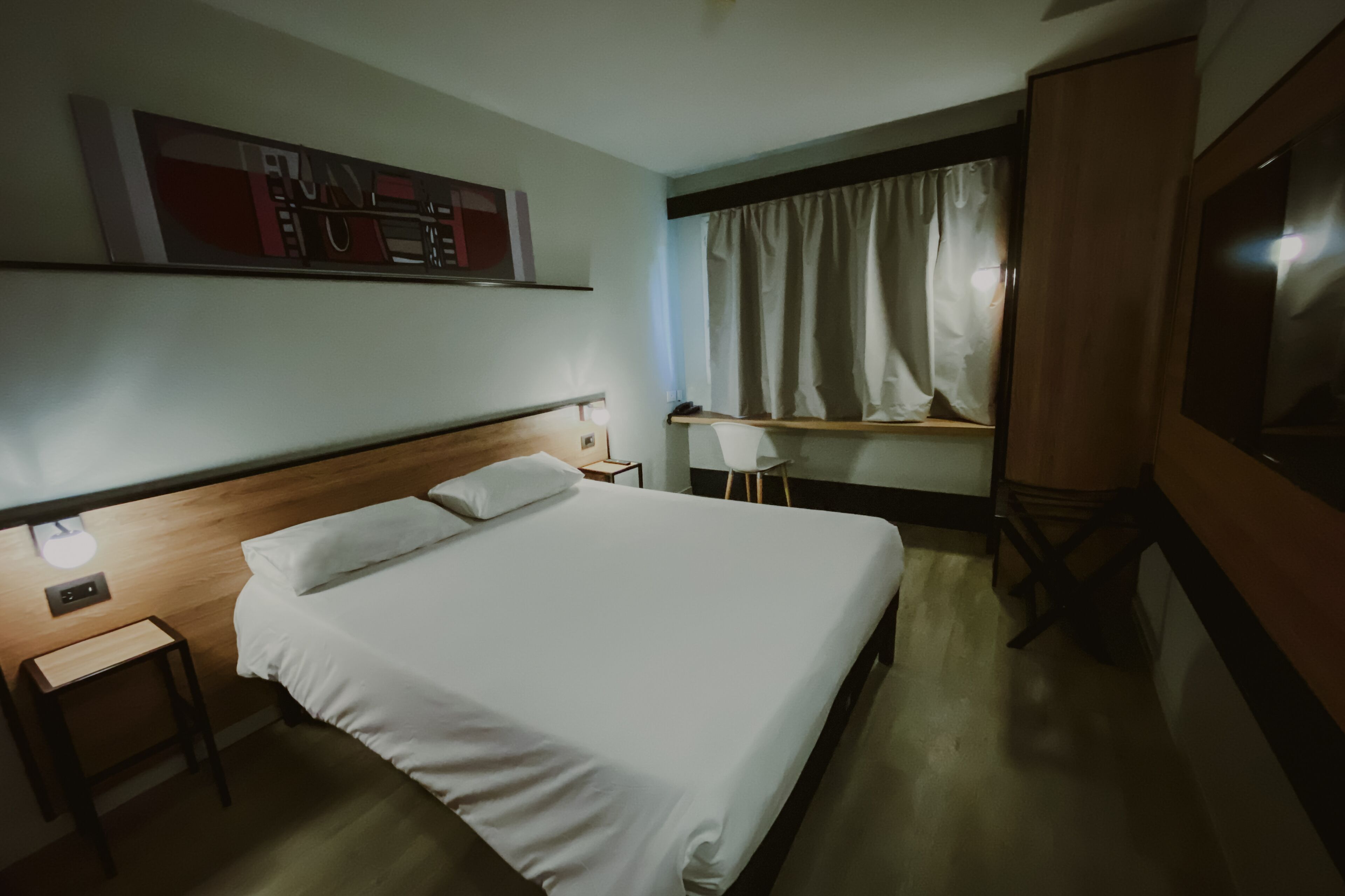 Een hotelkamer met een groot bed, een bureau, een stoel, een klein tafeltje en een televisie.