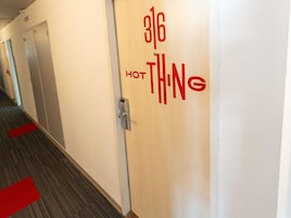 Un pasillo con una puerta que indica '316 HOT THING' y una alfombra roja en el suelo.