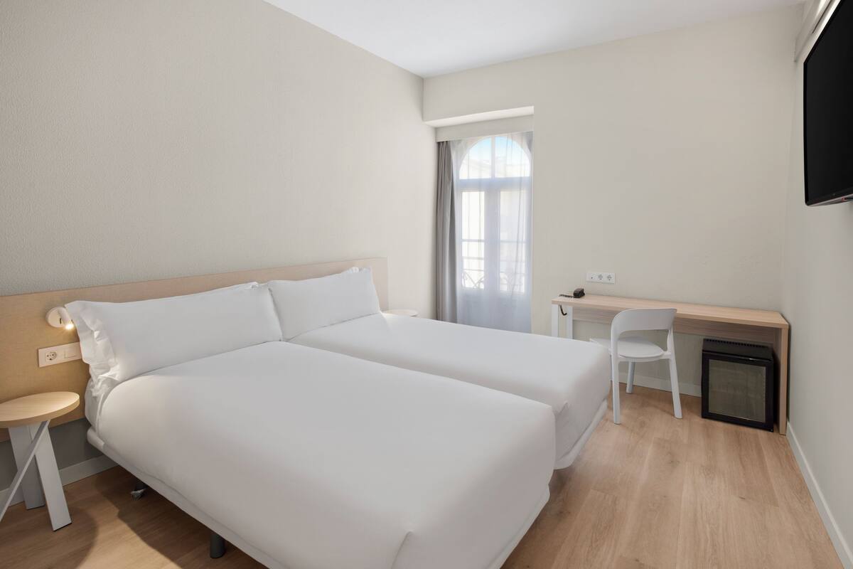 Habitación de hotel con dos camas, un escritorio, una silla y un televisor.