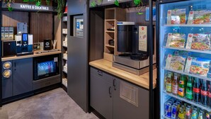 Uma área de cozinha compacta com cafeteira, aparelho de bebidas e geladeira abastecida com alimentos e bebidas.