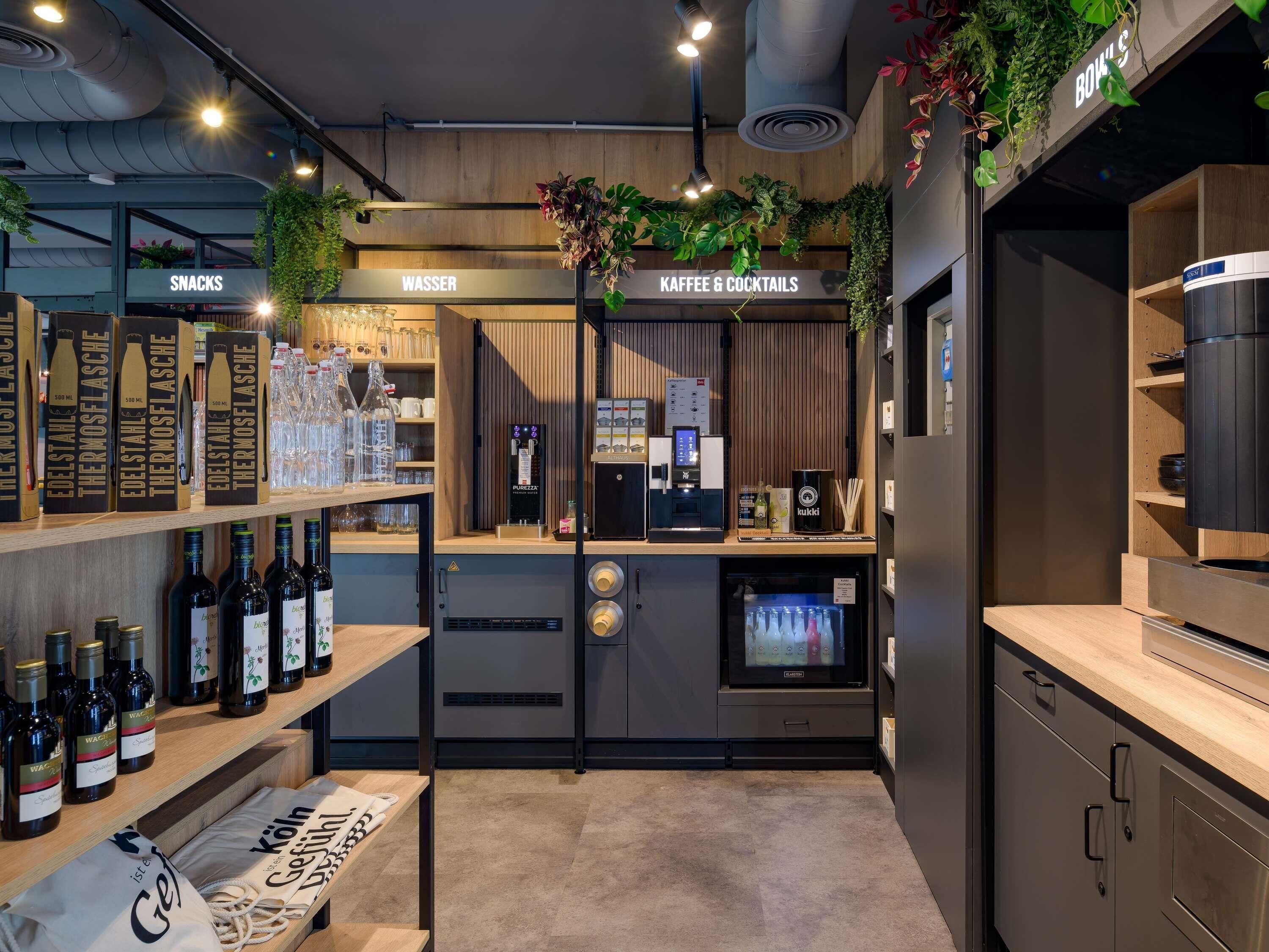 Zona de bar con estantes de bebidas embotelladas, una máquina de café y un letrero que anuncia aperitivos y agua.