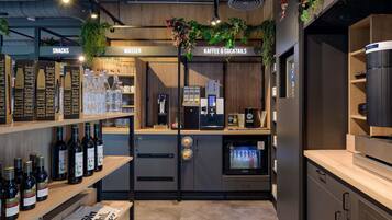 Zona de bar con estantes de bebidas embotelladas, una máquina de café y un letrero que anuncia aperitivos y agua.