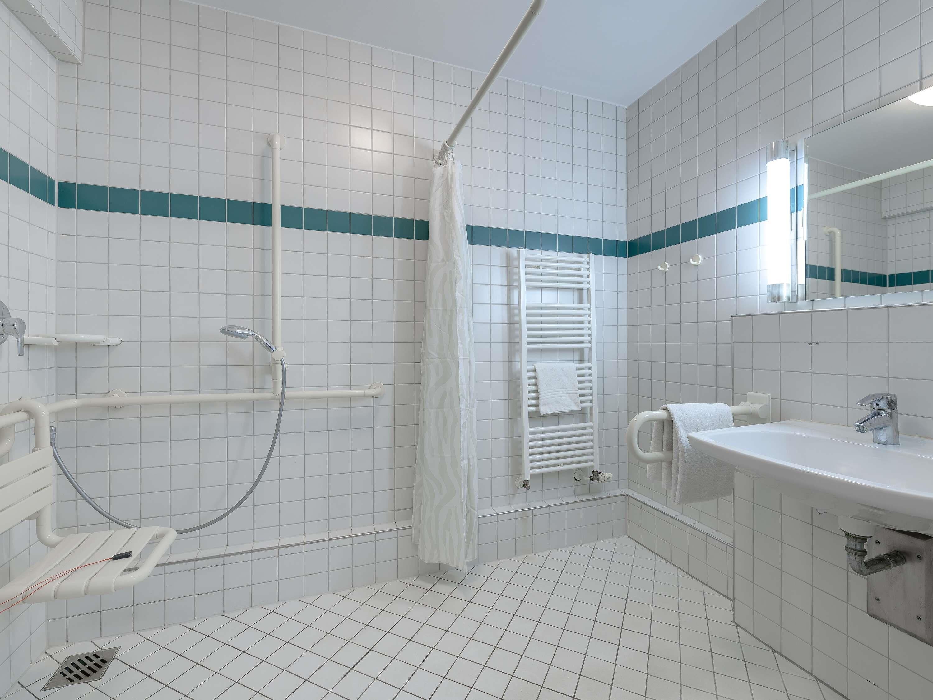 A bathroom with white tiled walls, a shower with a white curtain, a white sink, and a mirror.
