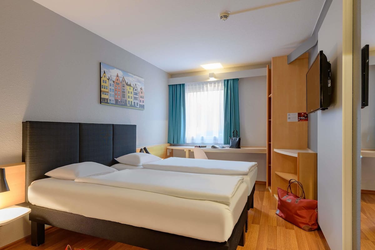 A hotel room with two beds, a desk, a chair, a TV, and a painting on the wall.