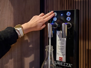 A hand operating a water dispenser with a label indicating options for still water and sparkling water. - ibis Köln Frechen (Frechen)