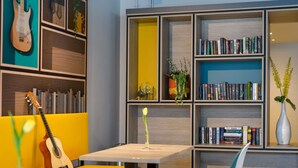 Um espaço de leitura moderno com uma estante, um violão e um vaso com flores.