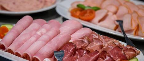 Variedad de carnes cortadas en platos, incluyendo jamón y prosciutto, con un tenedor y cuchillo al lado.