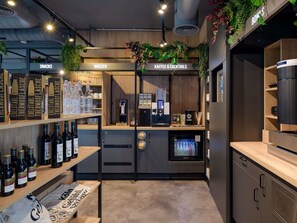 A bar area with shelves of bottled drinks, a coffee machine, and a sign for snacks and water. - ibis Köln Frechen (Frechen)
