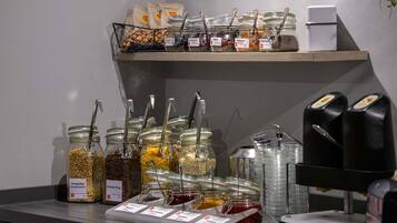 Un espace de restauration en libre-service proposant divers aliments présentés dans des bocaux et des sachets, ainsi qu’une machine à café et un distributeur d’eau.