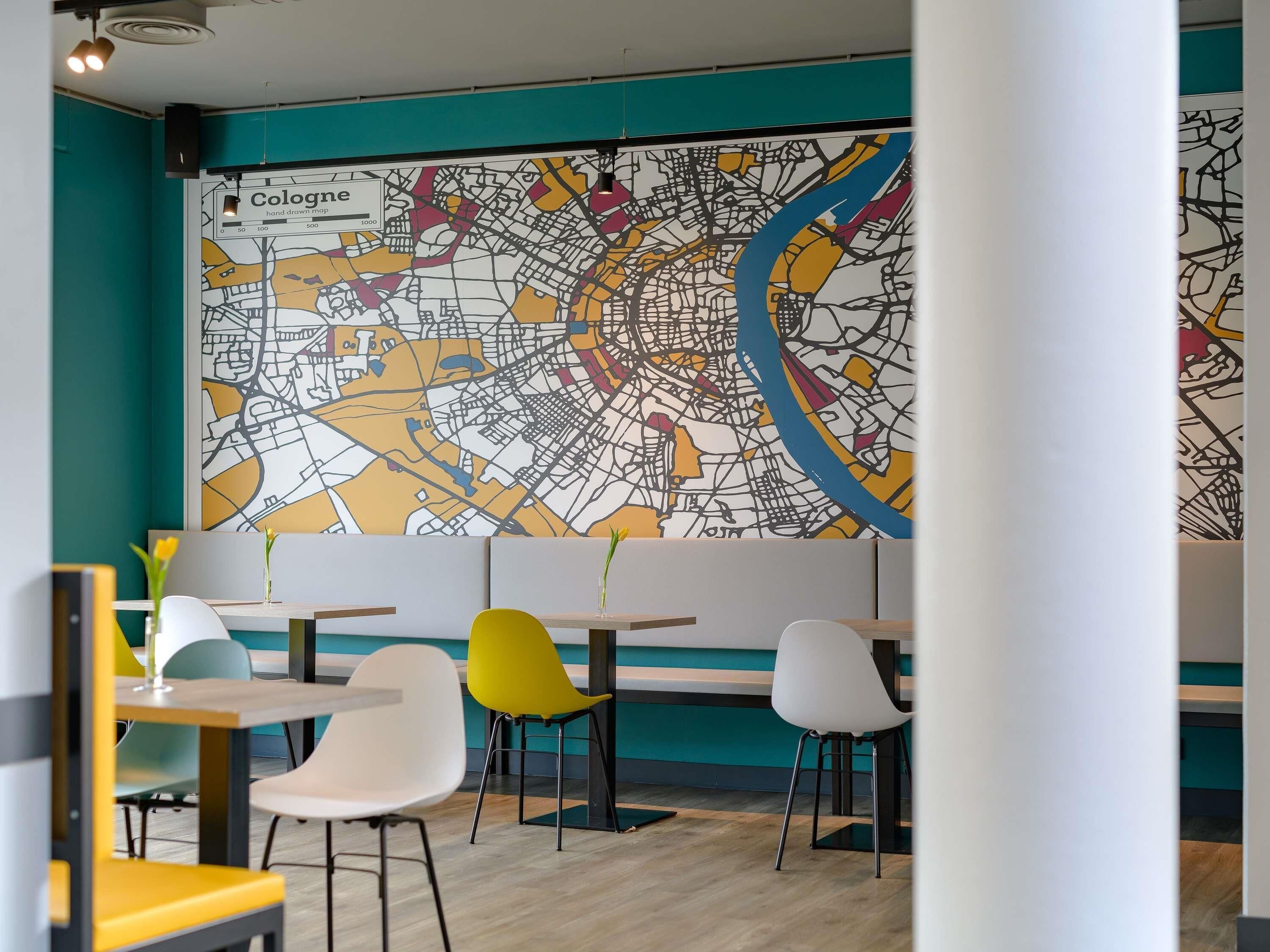 Un restaurante con un gran mapa mural, sillas coloridas y una pared de acento color turquesa.