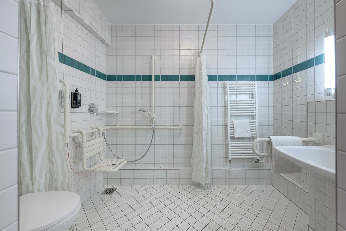A bathroom with a white toilet, a shower with a white curtain, a white sink, and a towel rack.
