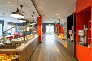 Un moderno vestíbulo de hotel con una larga recepción, una máquina de café y una zona de bufé con frutas y verduras.
