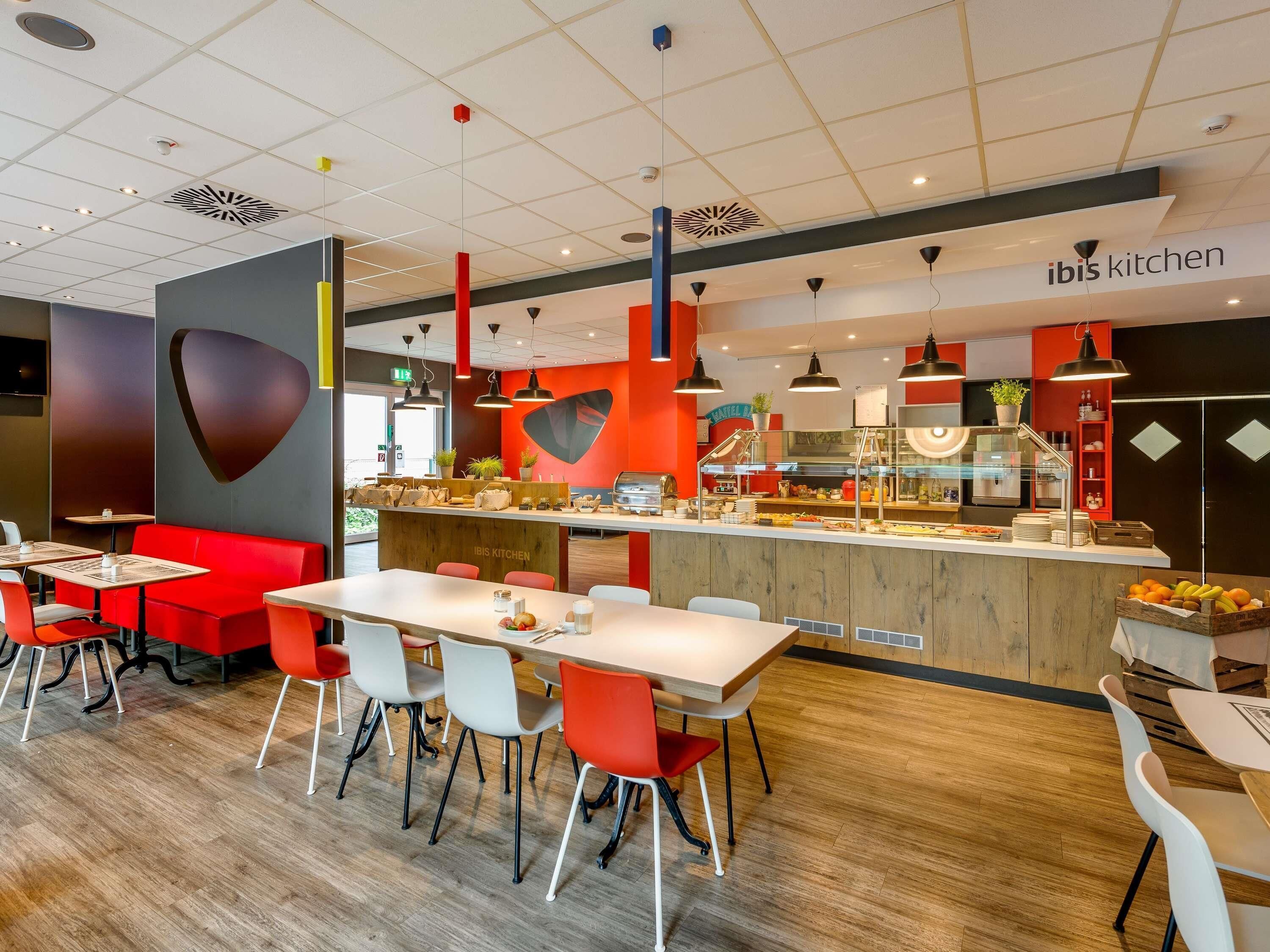 A modern restaurant interior with red and white decor, a counter with food display, and seating arrangements.