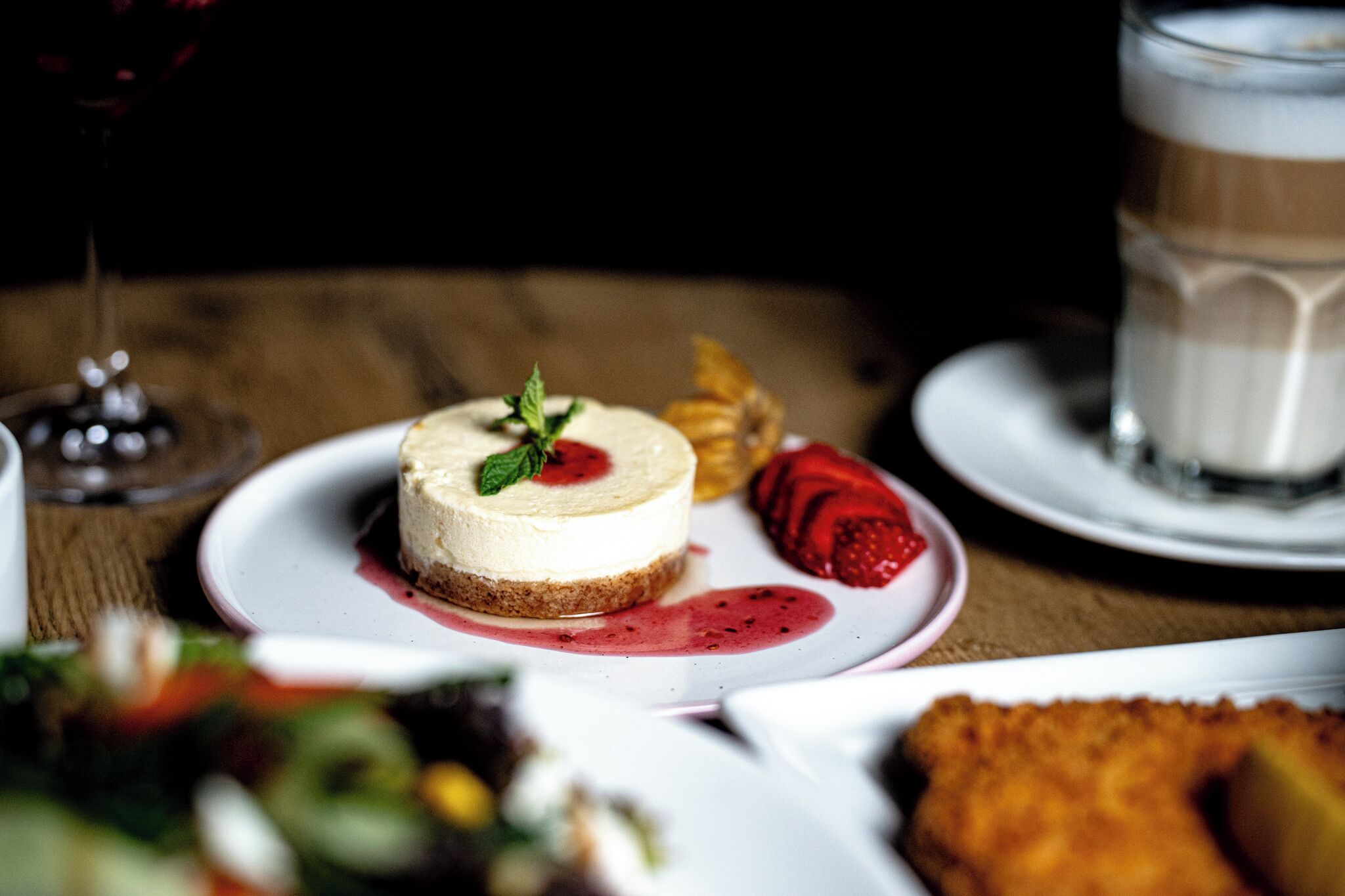 A dessert plate with cheesecake, strawberries, and a mint garnish.