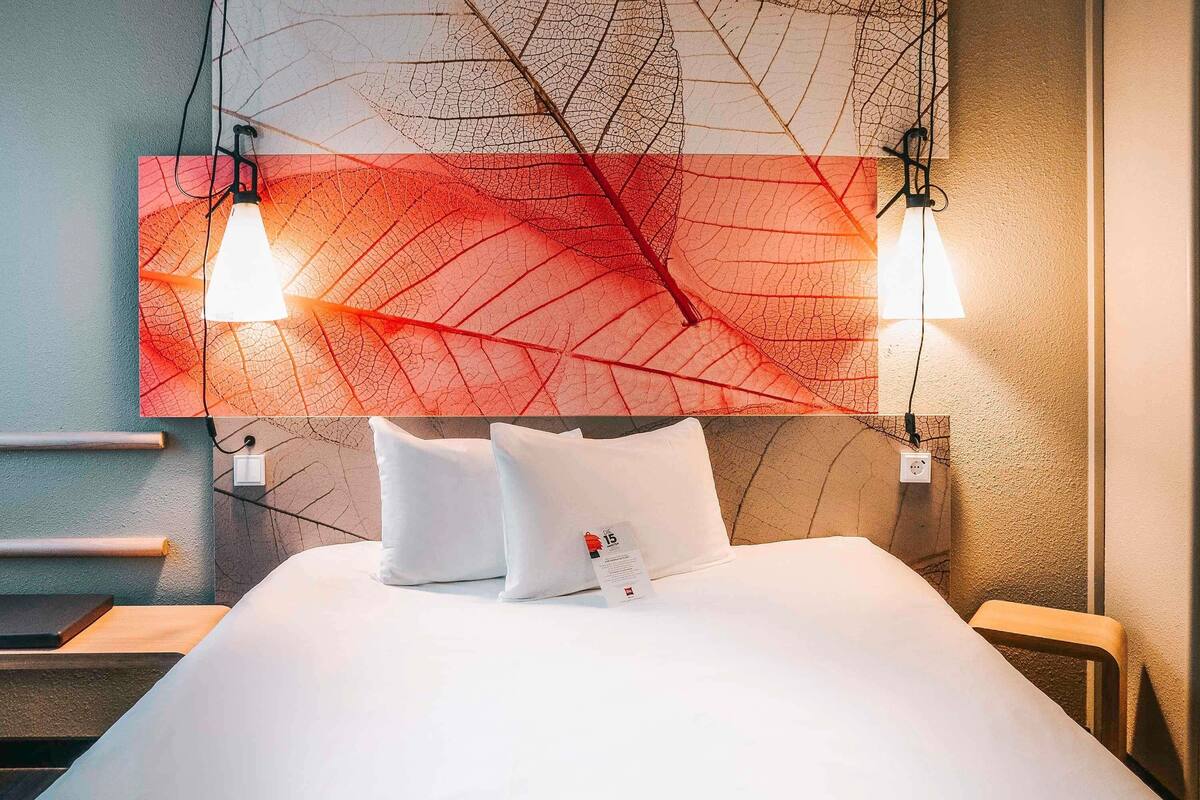 A hotel room with a large bed, two bedside lamps, and a wall-mounted artwork.