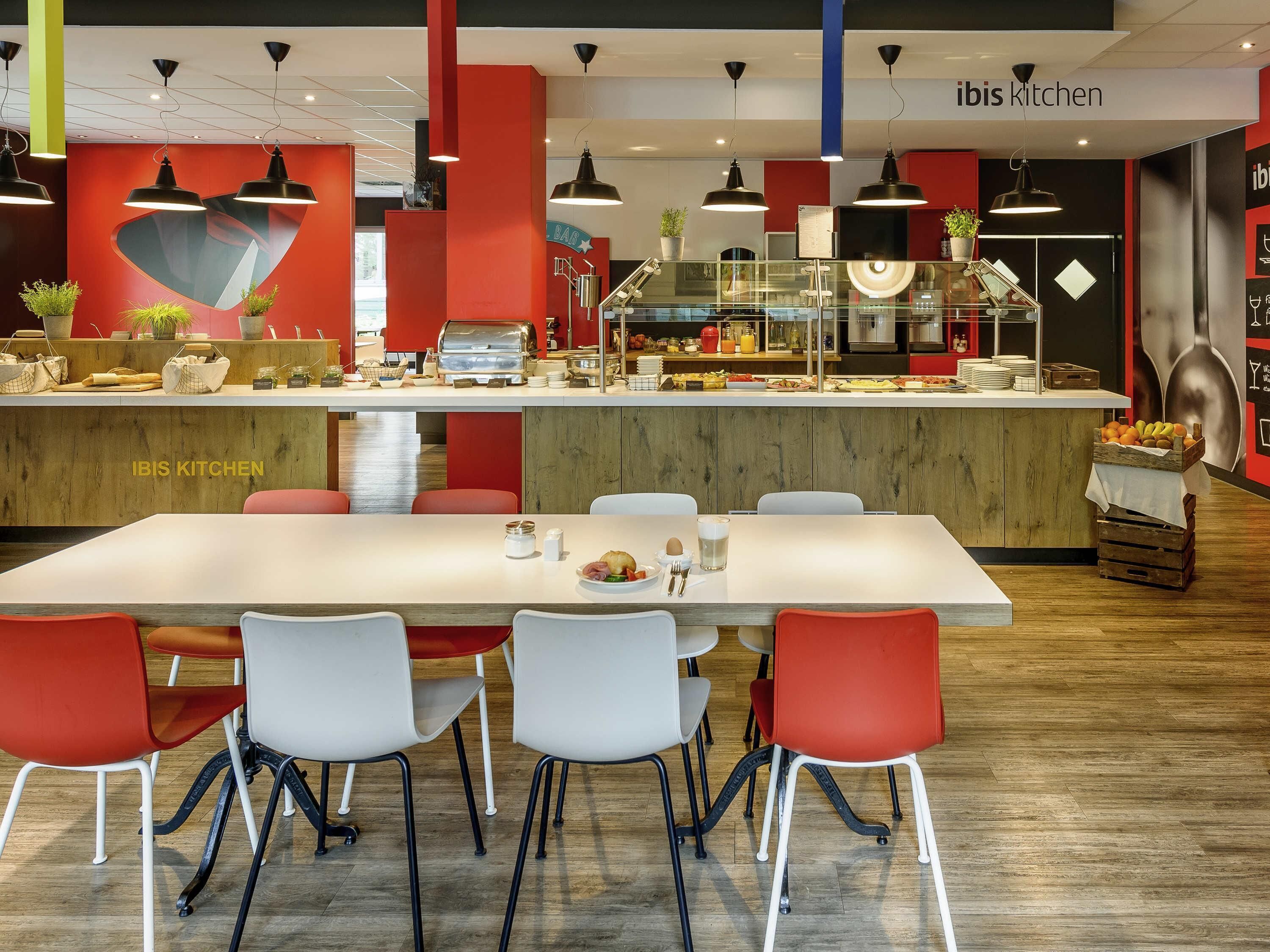 A modern kitchen area with a counter, seating, and a sign reading 'IBIS KITCHEN'.