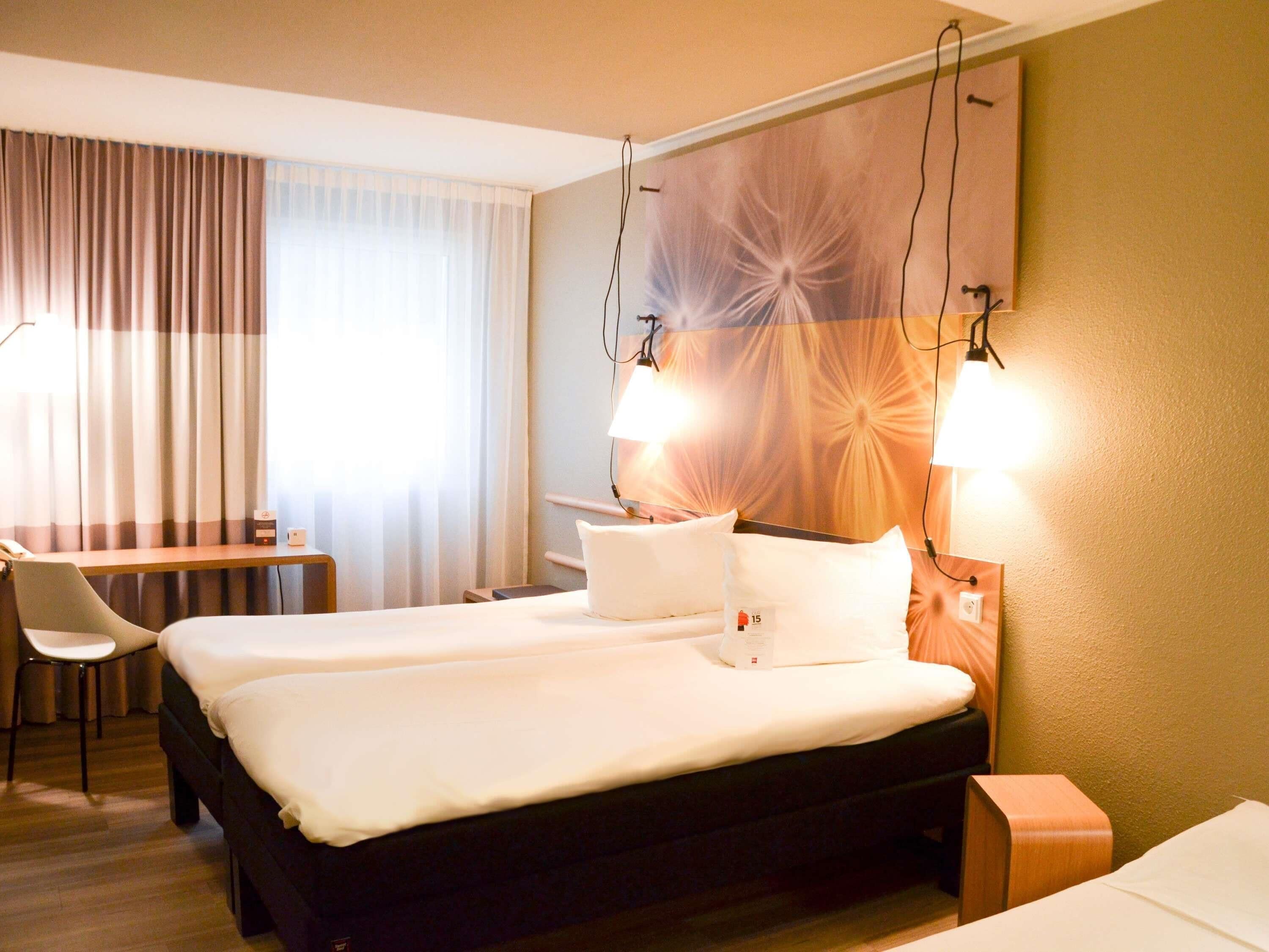 Ein Hotelzimmer mit zwei Betten, einem Schreibtisch, einem Stuhl und einer großen Wanddekoration.