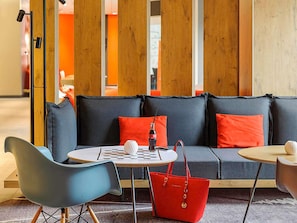 Un espace détente moderne avec un canapé gris, des coussins rouges, une table ronde, une chaise bleue et un sac à main rouge.