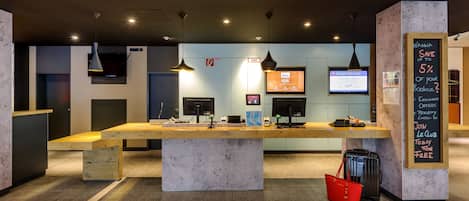 A modern reception desk with a wooden counter, a large central table, and a blackboard with promotional offers.