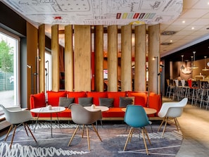 A modern interior with a red sofa, round tables, and wooden columns. - ibis Frankfurt Airport (Kelsterbach)
