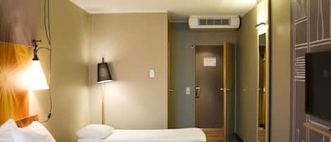 A hotel room with a bed, bedside lamp, air conditioning unit, and a mirror.