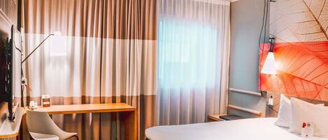 Habitación de hotel con cama, escritorio, silla, televisor y lámpara de pared.