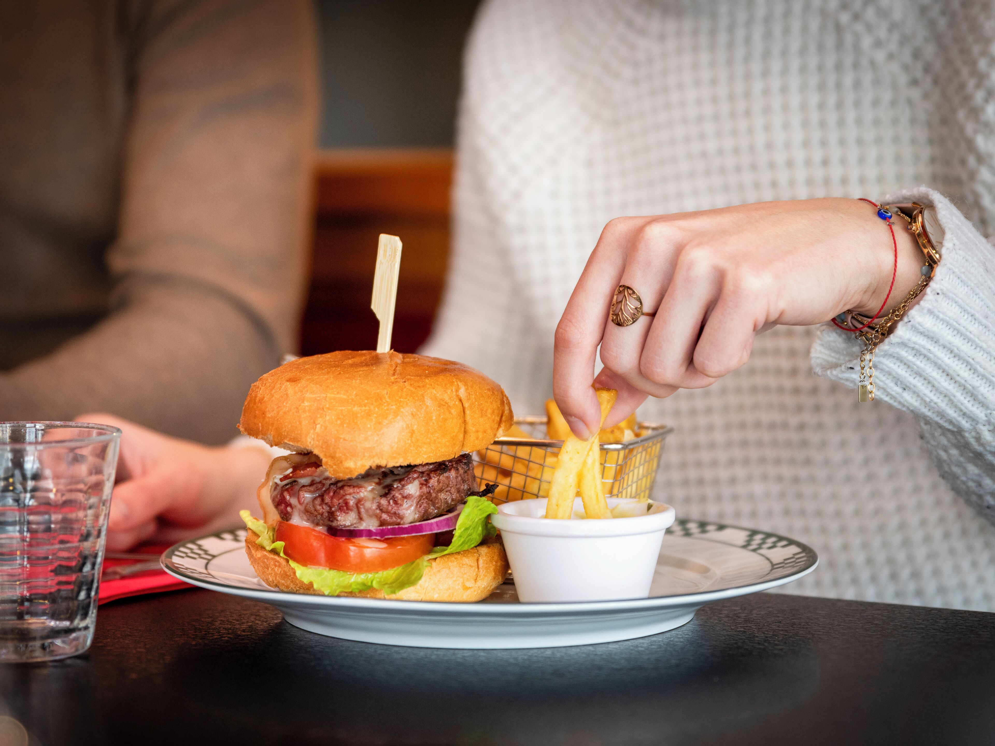 Un piatto con un hamburger e patatine fritte, un bicchiere d'acqua e una persona che indossa un anello.