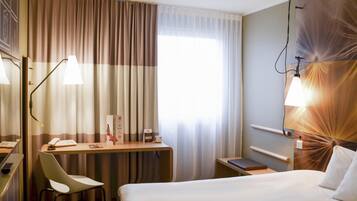 Habitación de hotel con cama, escritorio, silla y lámpara fijada a la pared.