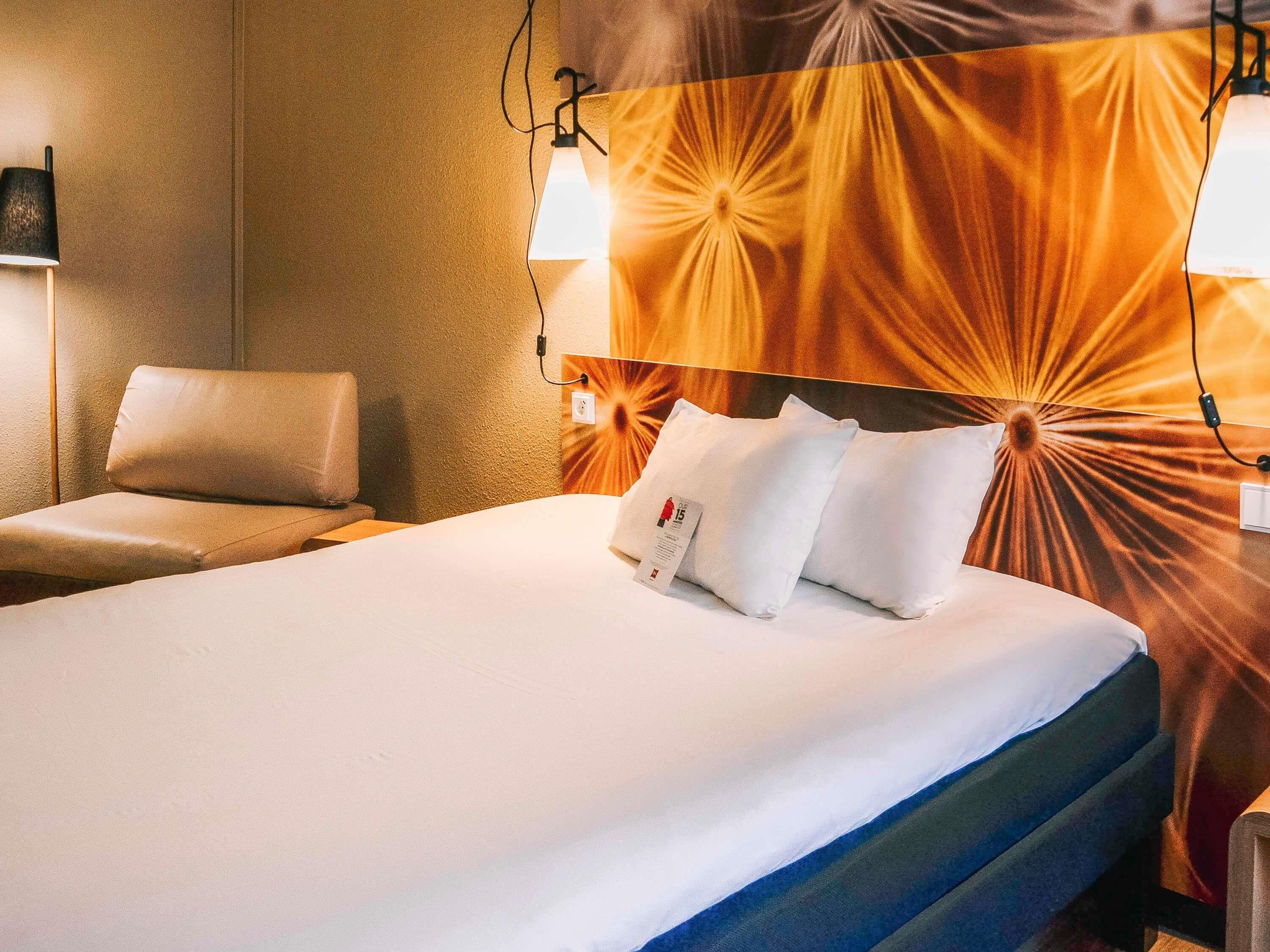 Ein Hotelzimmer mit Bett, Stuhl und Wandlampe.