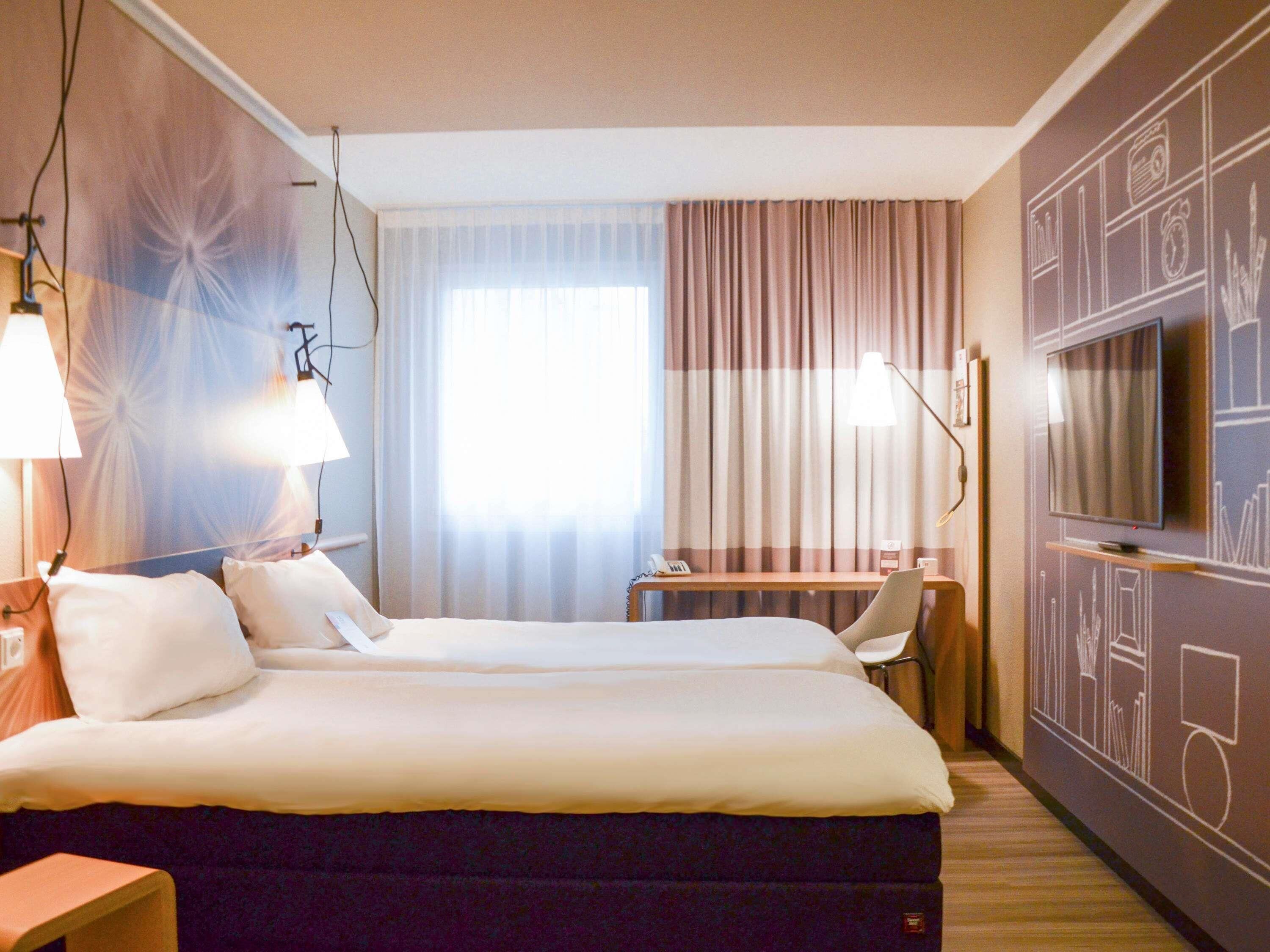 A hotel room with a bed, a desk, a TV, and a lamp.