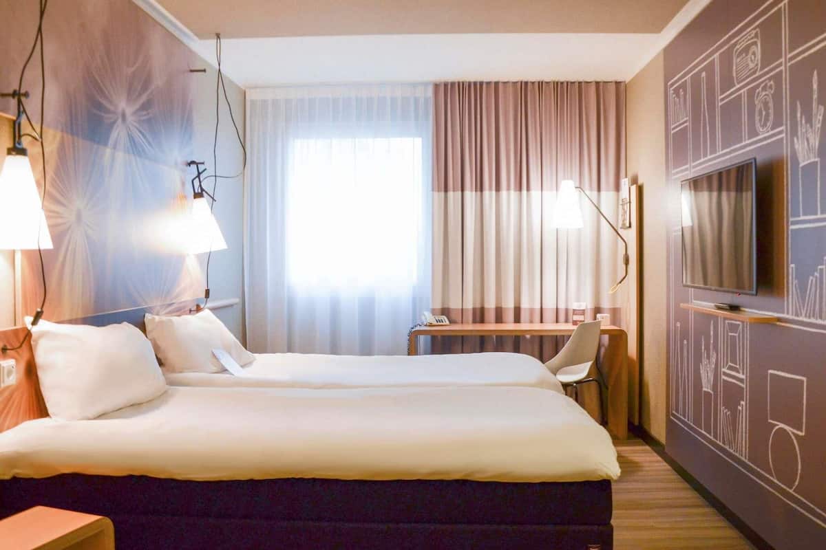 Une chambre dâhĂŽtel avec un lit, des lampes de chevet, un bureau, une tĂ©lĂ©vision et un rideau.