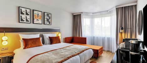 A hotel room with a large bed, a desk with a coffee maker, a chair, and a TV.
