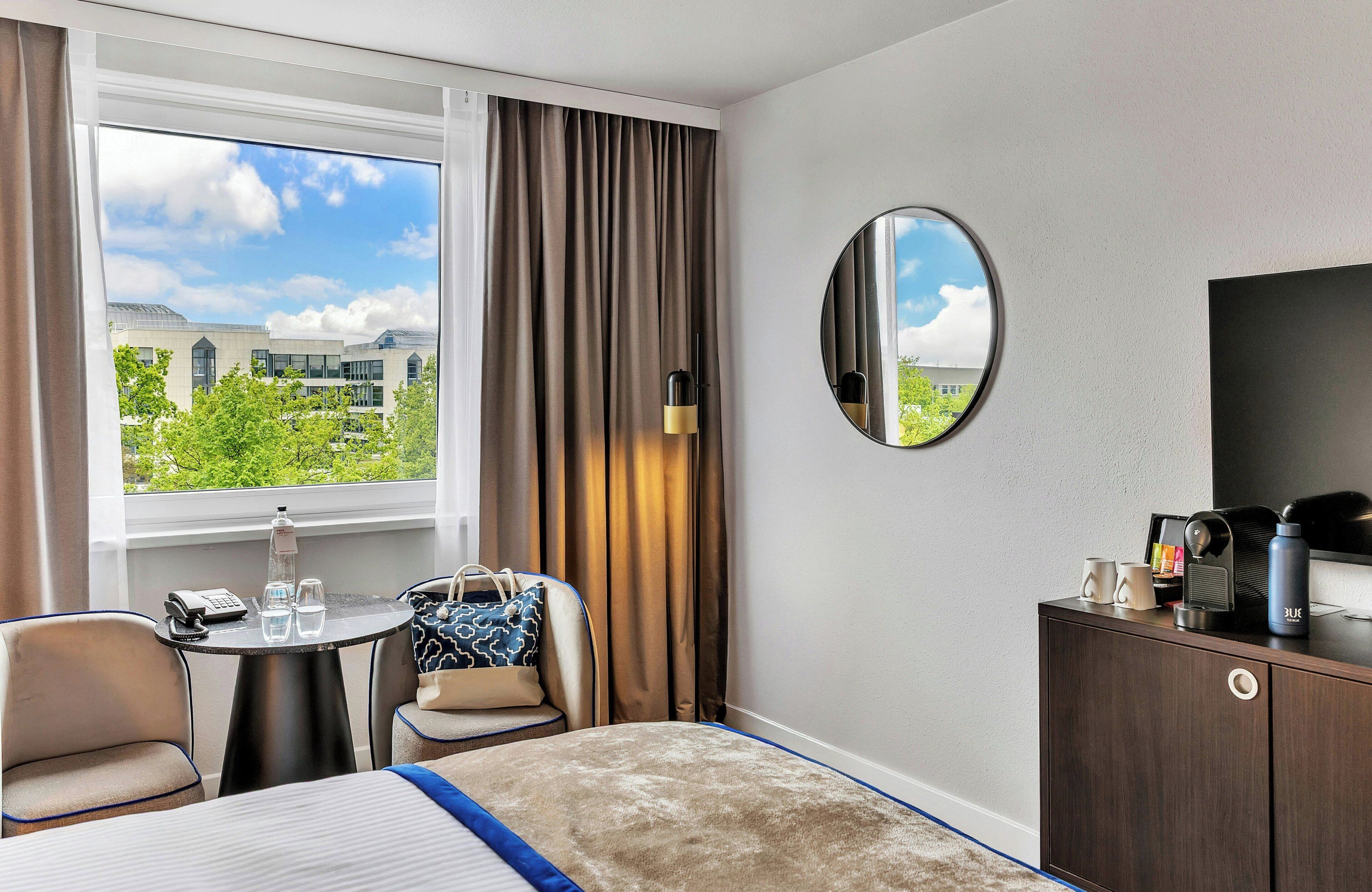 A hotel room with a bed, a desk, a chair, a TV, and a window with curtains.
