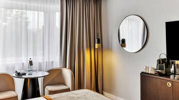 Habitación de hotel con una cama, un espejo redondo, un escritorio con teléfono, una lámpara y un mueble con televisor.
