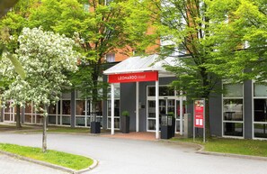L’entrée d’un hôtel, avec une enseigne rouge, des portes en verre et une allée pavée.