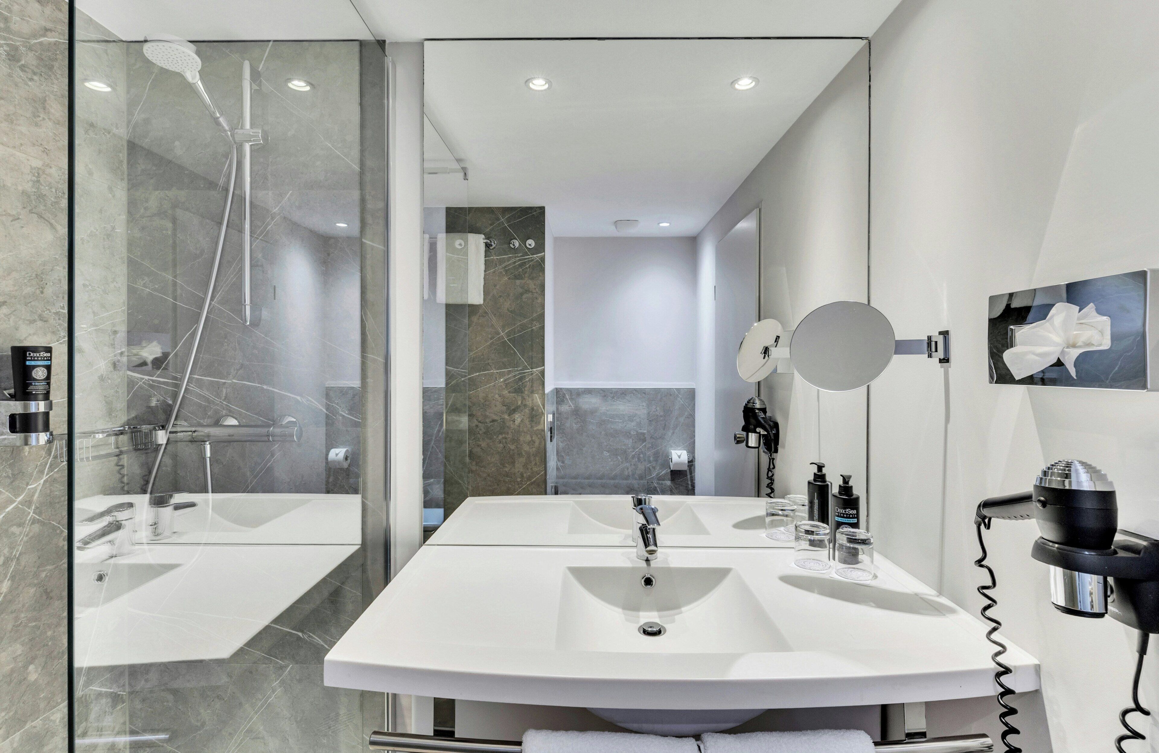 A modern bathroom with a glass-enclosed shower, two sinks, a hairdryer, and a mirror.